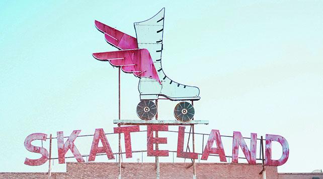 Photo of retro neon sign with winged roller skate and the word SKATELAND above a brick skating rink