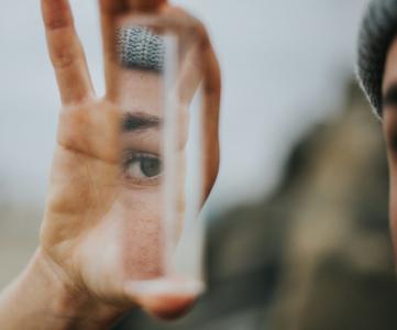 Person holding up a sliver of a mirror and seeing a partial reflection of her face.