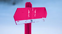 Fuschia pink hiker sign pointing both right and left contrasting against a white and blue snow scene